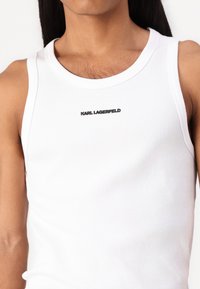 White ribbed tank top featuring a round neckline and black "KARL LAGERFELD" logo on the chest. Lightweight, form-fitting material.
