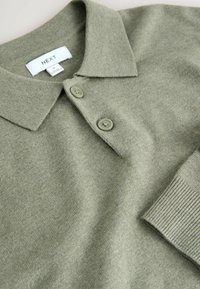 Olijfgroene polo-shirt van zacht, textuurstof met een kraag, twee knoopsluitingen en ribgebreide mouwuiteinden. Merkenlabel zichtbaar.