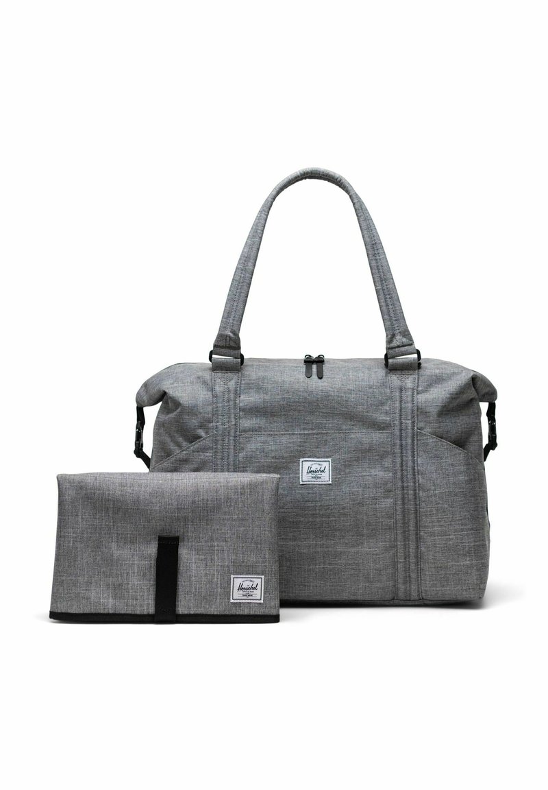 Sac de sport en tissu gris avec deux poignées supérieures et un matelas à langer plié assorti, tous deux portant des étiquettes de la marque Herschel.