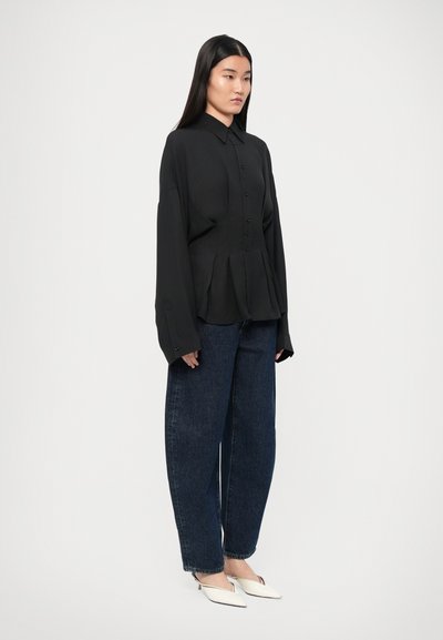 Must have pikkade varrukatega must nööbiga särk koos krae ja volditud detailidega, kombineeritud lõdvema tumehallide teksade ja valgete slip-on kingadega.