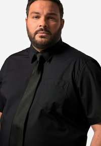 Camisa negra de mangas cortas con un bolsillo en el pecho y una corbata negra de satén. La tela tiene una textura suave y un diseño de ajuste regular.