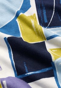 Pamut textil színes geometrikus mintával, kék, zöld, lila és tengerész kék formákkal fehér háttérrel, texturált felülettel.