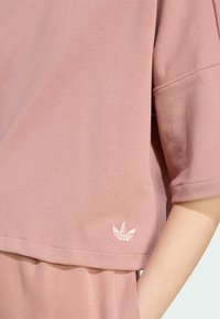 Ružový bavlnený sveter s krátkymi rukávmi, s diskrétnym vyšitým logom na leme a uvoľneným strihom. Mäkká textúra, minimalistický dizajn.