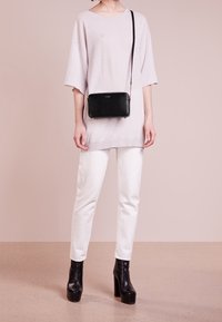 Czarna skórzana torba na ramię o gładkiej fakturze, zamykana na zamek błyskawiczny, z długim paskiem. Nosi się ją na jasnoszarej, luźnej bluzce oraz białych dżinsach.