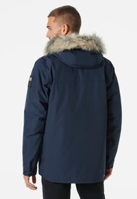 Chaqueta aislante de color azul marino con cuello de pelo sintético. Cuenta con capucha, mangas largas y un detalle texturizado en los parches de los hombros.