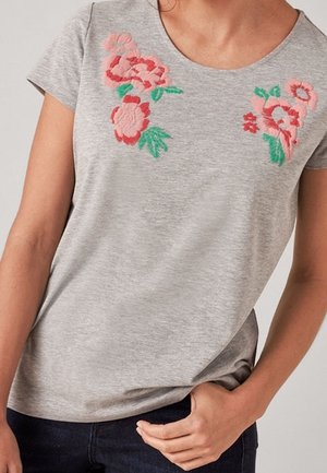 Szary T-shirt z krótkim rękawem, ozdobiony kwiatowym haftem w różowym i zielonym kolorze wokół dekoltu. Miękka tekstura, okrągły dekolt, luźny krój.