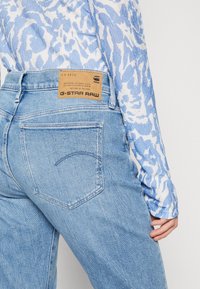 Ljust blå denimjeans med en klassisk femfickdesign, som har en synlig läderetikett på baksidan av midjan och subtila sömdetaljer.