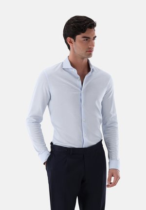 Hellblaues Langarmhemd mit Button-Down-Kragen, glatter Oberfläche und dezenten Nähten, getragen mit dunklen, taillierten Hosen.