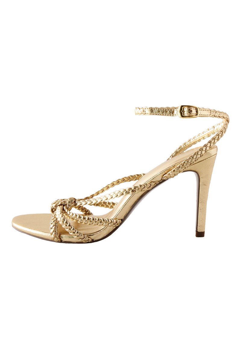 Sandale à talon haut dorée avec lanières tressées, bout ouvert et boucle à la cheville. Finition métallique avec texture lisse et design de talon fin.