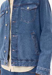 Denim jakna svijetloplave boje, s dva džepa na prsima, metalnim gumbima i kontrastnim šavovima. Mekana tekstura s ležernim krojem.