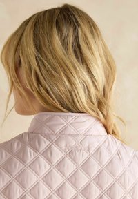 Helle rosa gesteppte Jacke mit einem Rautenmuster und einem Kragen; das "Joules"-Logo ist auf dem Rücken eingestickt.