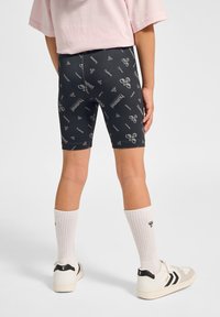 Svarta cykelbyxor med ett upprepat grått logomönster, ihop med vita ribbade strumpor och vita sneakers med svarta detaljer.