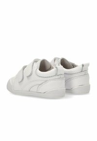 Zapatos de cuero blancos con punta redondeada, correas de velcro y suelas de goma texturizadas. Costuras acentuadas y detalles de diseño mínimos.