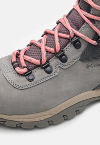 Stivale da trek in suede grigio con lacci intrecciati rosa, inserti in rete e hardware nero; presenta una suola in gomma testurizzata con un motivo esagonale.