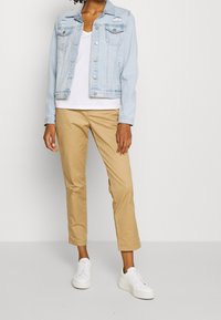 Světle modrá denimová bunda s distressed detaily, bílý tričko, béžové chinos a bílé tenisky, zdůrazňující neformální vrstvený styl.