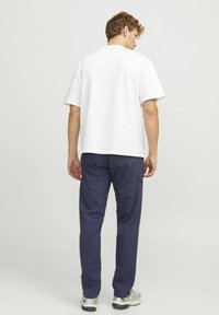T-shirt bianco in cotone a maniche corte, indossato con pantaloni larghi blu scuro. Presenta una vestibilità rilassata e un design semplice.
