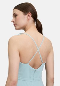 Jasnoniebieska sukienka z zamekiem na plecach, otwartym plecami i krzyżującymi się ramiączkami. Gładka tkanina i dopasowana sylwetka.