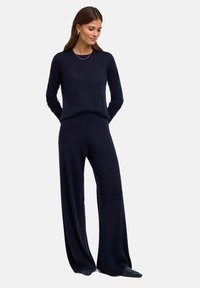 Granatowy sweter dzianinowy i zestaw szerokich spodni. Miękka faktura, długie rękawy i luźny krój. Minimalistyczny design bez widocznych wzorów czy elementów metalowych.