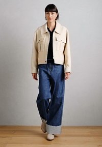 Kremfarget cropped jakke med store frontlommer, kombinert med vide jeans med frynsete kant og beige ankelstøvler.