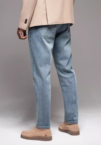 Jeans de mezclilla azul claro con un corte relajado, que cuentan con dos bolsillos traseros y una ligera textura de lavado. Combinados con botines de ante en tono marrón claro.