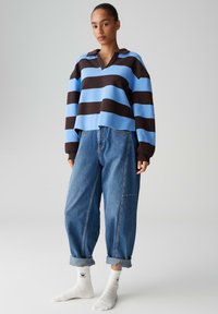 Maglione oversize a righe blu e marroni con colletto, abbinato a jeans in denim a taglio largo e calzini bianchi con motivo a cuori.