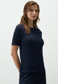 Top corto blu navy con maniche corte realizzato in un tessuto testurizzato con un motivo in rilievo. Collo rotondo e vestibilità rilassata, orlo rifinito.
