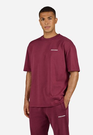 Maroon cotton t-shirt with short sleeves, round neck, and white “PEGADOR” logo. Fabric appears lightweight and smooth.