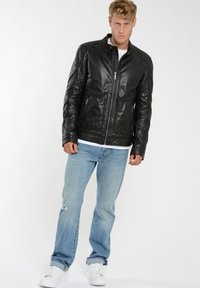 Sort læderjakke med lynlås, ribbede skulderdetaljer og forlommer, parret med lyseblå jeans og hvide sneakers.