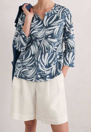 Top de estampado floral en azul marino y blanco con cuello redondo y mangas tres cuartos, combinado con pantalones cortos de lino crema.