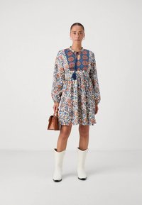 Suknelė su gėlių raštu, ilgomis rankovėmis, siaurintu liemeniu ir tamsiai mėlynomis detalėmis. Derinama su baltais vakarų stiliaus batais ir ruda rankine.