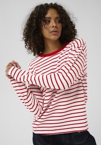 Valgete puuvillaste punaste horisontaaltriipudega pikkade varrukatega särk, ümar kaelus ja lõdvestunud istuvus. Varrukad on üles keeratud mansettidega.