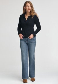 Czarny sweter w splot kablowy z kołnierzykiem, w zestawieniu z jasnoniebieskimi dzwonami i brązowymi botkami za kostkę. Teksturowana tkanina, dopasowany fason.