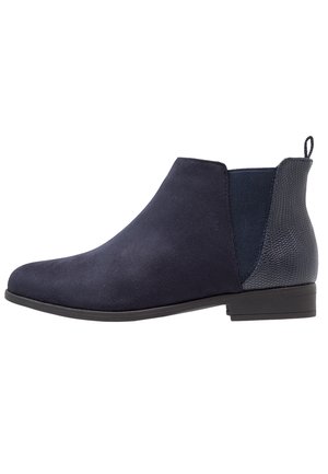 Bottine en suède bleu marine avec panneau arrière texturé, empiècement élastique sur le côté, talon bas et languette pour un enfilage facile.