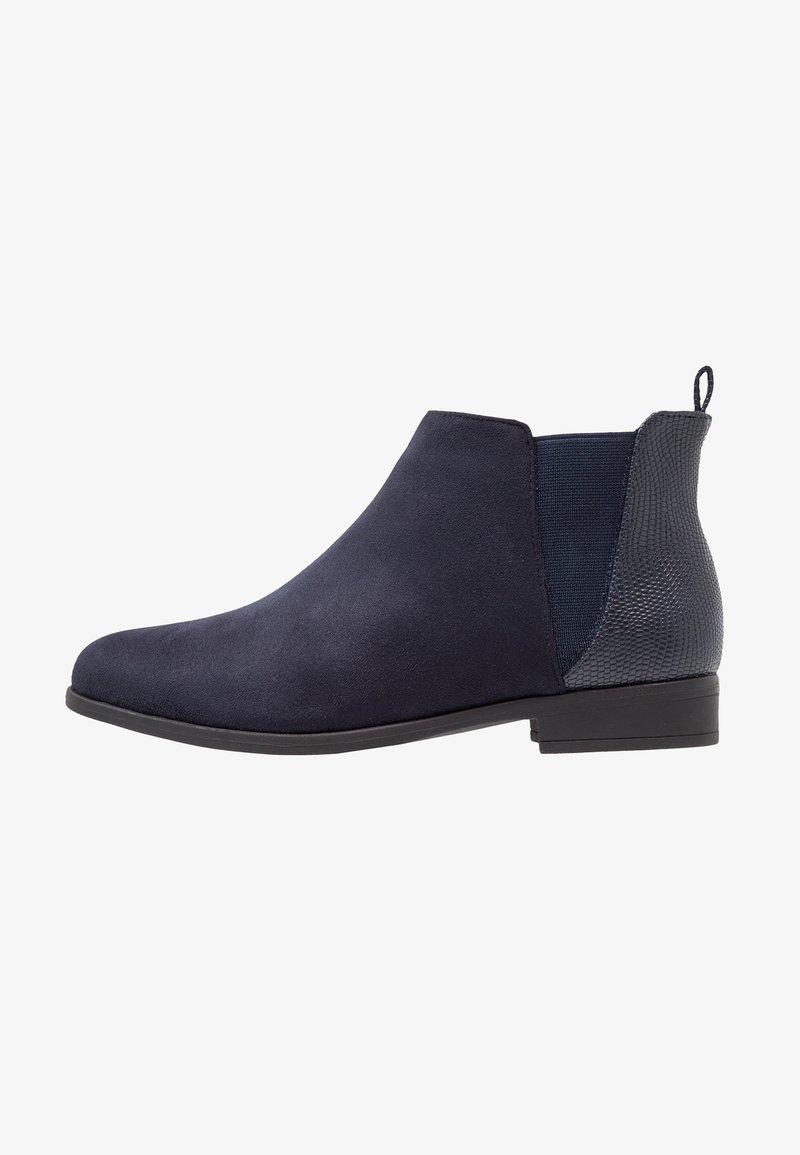 Bottine en suède bleu marine avec panneau arrière texturé, empiècement élastique sur le côté, talon bas et languette pour un enfilage facile.