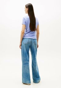 T-shirt corto a maniche corte di colore viola chiaro abbinato a jeans in denim blu a vita alta e gamba larga. Texture del tessuto liscia con tasche posteriori classiche.