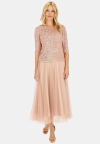 Lśniący top w różowym złocie z cekinami i rękawami o długości trzech kwart, zestawiony z zwiewną beżową spódnicą z tiulu. Miękka faktura, dopasowany krój, elegancki design.