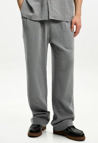 Graue strukturierte Hose mit lockerer Passform, die ein dezentes Rippmuster aufweist. Kombiniert mit schwarzen Schuhen und einem passenden grauen Oberteil.