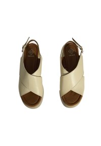 Beige leather sandals with crossed upper straps and open toe, featuring a brown insole and buckle detailing at the heel.