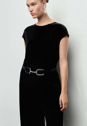 Jumpsuit en velours noir avec des manches courtes. Doté d'une large ceinture avec des ferrures en argent. Texture lisse, design ajusté mettant en valeur la taille.