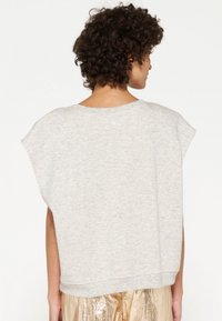 Felpa grigia a maniche corte con vestibilità rilassata, realizzata in tessuto morbido; presenta un colletto rotondo e un colore uniforme con una texture liscia.