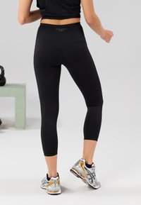 Black capri leggings featuring a high waistband and smooth texture, paired with reflective accents and grey running shoes with gold details.