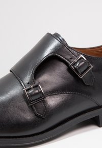 Chaussure en cuir noir avec une finition lisse, des accents à double boucle et un bout arrondi. Semelle robuste avec un talon léger pour plus de soutien.