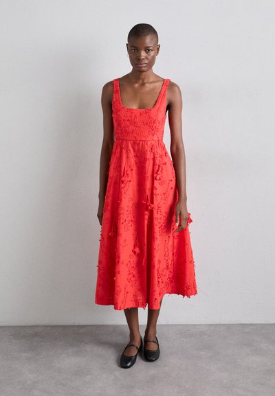 Abito rosso con spalline a sottile, ricamato con motivi floreali, forma ad A, lunghezza a metà polpaccio e frange decorative; abbinato a scarpe flat nere.