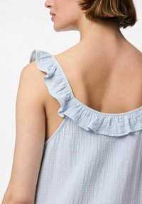 Gaiši zila bezpiedurkņu blūze ar ruffles plecu detaļu, kas izceļas ar teksturētu, mīkstu audumu un brīvu piegriezumu aizmugurē.