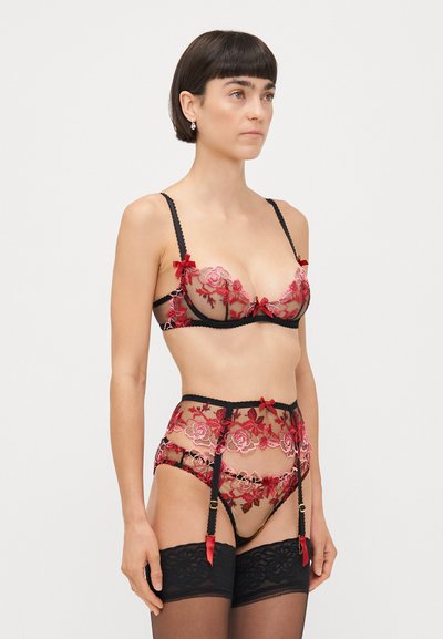 Ensemble de lingerie en résille noire transparente, brodé de fleurs rouges et avec des finitions noires. Comprend des nœuds sur le soutien-gorge et le porte-jarretelles, accompagné de bas en dentelle noire.