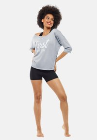 Gray, off-shoulder top with white text reading "First, iced coffee" paired with black shorts. The fabric appears soft with a loose fit.