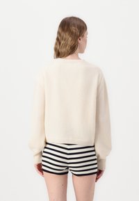 Chunky creamfarvet strikket sweater med ribbede manchetter og kant, parret med sort-hvide stribede shorts. Blød tekstur og afslappet pasform.
