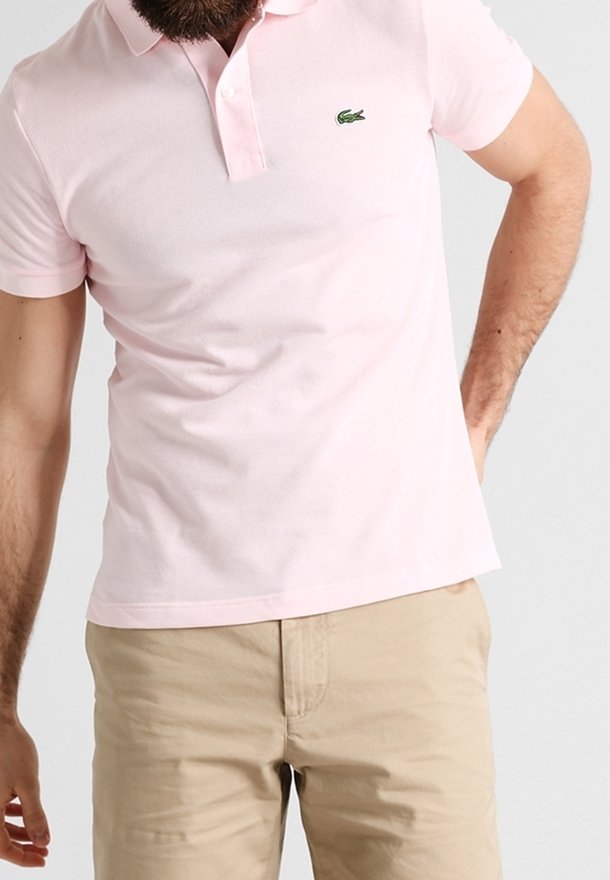 Polo shirt rose clair en coton, avec un col classique, des manches courtes et un logo brodé vert sur la poitrine gauche.