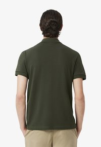 Olivgrön kortärmad polo med klassisk krage och en slät textur, med rak fåll och inga synliga mönster eller detaljer.