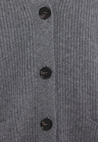 Tissu en maille côtelée grise avec trois boutons noirs alignés verticalement, chacun cousu avec quatre trous, sur le devant d'un vêtement.